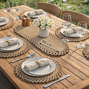 Könnte beinhalten: Ein Holztisch für sechs Personen im Freien, mit gewebten Tischsets und einem 80 cm langen Tischläufer. Jedes Gedeck umfasst einen weißen Teller, eine Leinen-Serviette und Besteck. Eine Vase mit weißen Blumen und Weingläsern vervollständigen die Szene.