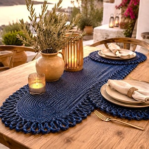 Puede incluir: Un camino de mesa de cuerda azul oscuro con textura trenzada y borde de bucles, sobre una mesa de madera con manteles individuales circulares a juego, platos de cerámica beige, servilletas de lino, tenedores dorados, un jarrón y candelabros.