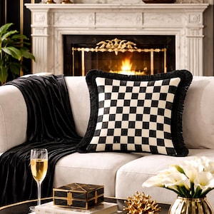 May include: A living room scene featuring a white sofa with a black and white checkered pillow with fringe. A black velvet throw is draped over the sofa. A coffee table displays books, a decorative box, and a gold accent piece.