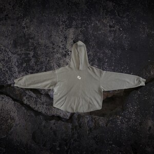 May include: A sage green hooded sweatshirt featuring long sleeves, a front kangaroo pocket, and a small white graphic logo centred on the chest. The garment has a relaxed fit with ribbed cuffs and a matching hood, showcasing a subtle distressed finish.