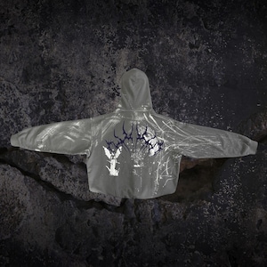May include: A grey hooded sweatshirt featuring a dark purple stylised graphic across the upper back, a white winged figure illustration on the lower left, and white splatter patterns extending across the right side of the garment.