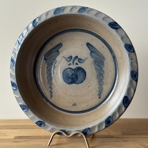 Puede incluir: Una taza de cerámica blanca con asa negra y el texto "But First, Coffee" en negrita negra. La taza se encuentra sobre un fondo borroso, sugiriendo un ambiente acogedor.