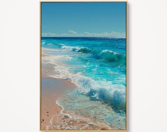 May include: A framed art print depicts a vibrant ocean scene. Turquoise waves crash onto a sandy beach under a clear blue sky. The artwork is encased in a gold-colored frame, adding a touch of elegance to the coastal landscape.