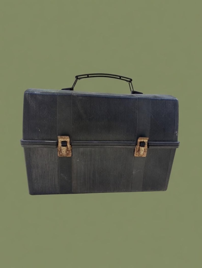 Puede incluir: Una fiambrera negra vintage con textura acanalada. La fiambrera tiene un asa negra y dos cierres met&aacute;licos de color &oacute;xido. La fiambrera es rectangular y parece estar hecha de pl&aacute;stico.