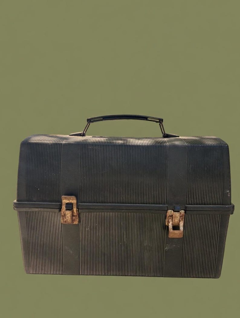 Puede incluir: Una fiambrera negra de estilo vintage con textura acanalada. La fiambrera tiene un asa negra y dos cierres met&aacute;licos oxidados. El fondo es de color verde oliva liso.