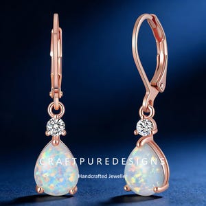 May include: Rose gold leverback earrings with pear-shaped opal drops and a small, round, clear gemstone accent. The earrings have the text "CRAFTPUREDESIGNS Handcrafted Jeweller".