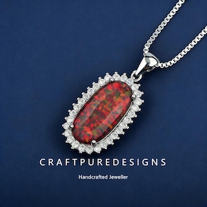 Puede incluir: Un collar con colgante de plata con una piedra preciosa ovalada roja y verde. La piedra preciosa está rodeada por un halo de pequeñas piedras transparentes. El collar está sobre un fondo azul. El texto "CRAFTPUREDESIGNS Handcrafted Jeweller" es visible.