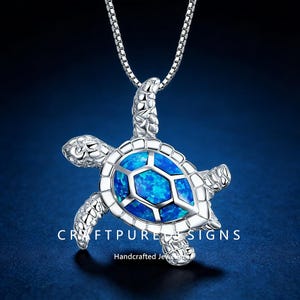 May include: A silver-colored turtle pendant necklace with a blue opal center. The turtle design has detailed flippers, head, and shell. The necklace is on a silver chain. The text "CRAFTPURE SIGNS" and "Handcrafted Jewels" are at the bottom.