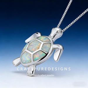 May include: A silver-colored turtle pendant necklace with an iridescent opal-like shell. The pendant is detailed with flippers, a head, and a chain. The text "CRAFT PURE DESIGNS" and "Handcrafted Jeweller" are visible.