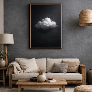 Puede incluir: Un cuadro enmarcado con una sola nube blanca y esponjosa sobre un fondo oscuro. La obra de arte cuelga sobre un sofá beige con cojines, una mesa de centro de madera y una alfombra tejida, creando un ambiente acogedor en el salón.