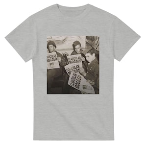 Puede incluir: Camiseta gris claro con un gráfico en tonos sepia de tres hombres leyendo periódicos. Los periódicos muestran las palabras "AVICULAR MOGGED" y "CLAVICULAR MOGGED". Una prenda informal.