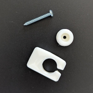 Könnte beinhalten: Eine Auswahl an Hardware-Komponenten, darunter eine silberne Schraube, ein weißes Kunststoffrad und ein weißer Kunststoffclip mit einer kreisförmigen Öffnung. Die Artikel sind auf einer dunklen Oberfläche angeordnet.