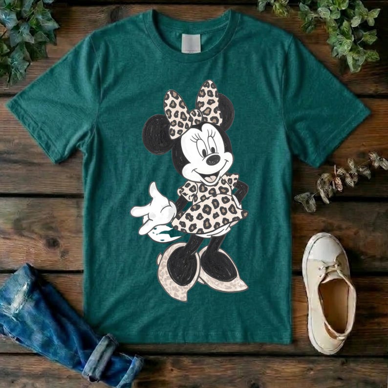 Op de afbeelding: Een donkergroen t-shirt met korte mouwen en een afbeelding van een cartoonmuisfiguur met een strik en een jurk met een beige en zwart luipaardprintpatroon. Het figuur heeft zwarte oren, een wit gezicht en witte handschoenen.