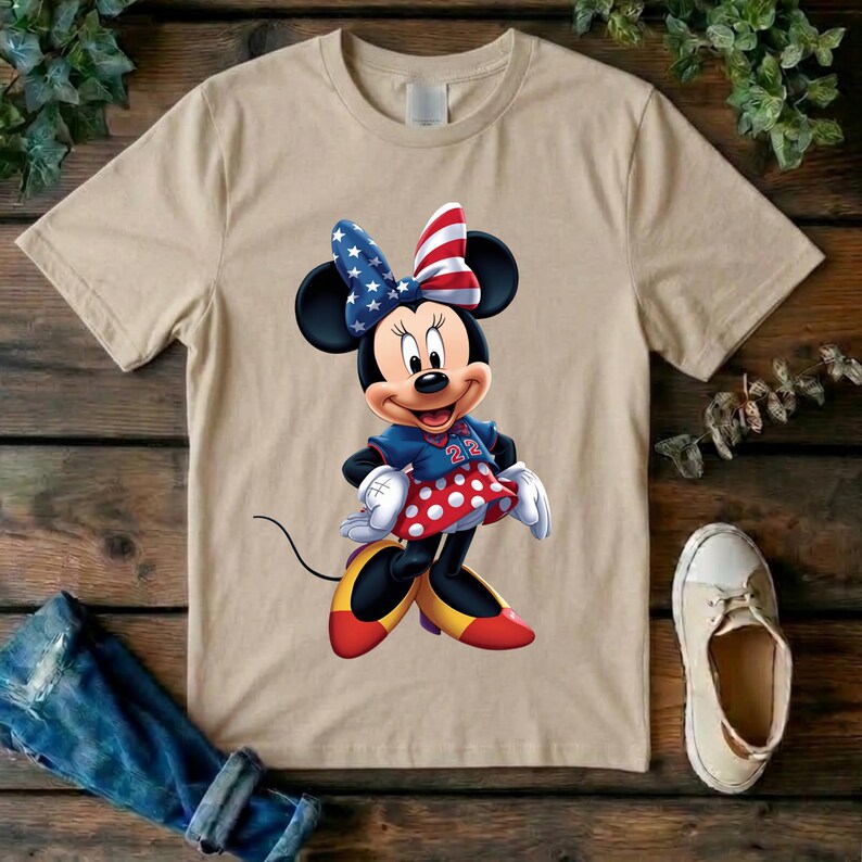 May include: A beige short-sleeve t-shirt featuring a graphic of Minnie Mouse wearing a patriotic bow with stars and stripes, a blue top with the number 22, a red and white polka dot skirt, and yellow shoes with red accents on a plain background.