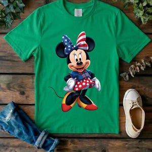 May include: A bright green short-sleeved t-shirt featuring a graphic of Minnie Mouse wearing a patriotic bow with stars and stripes, a blue jersey with the number 22, a red and white polka dot skirt, and yellow and red shoes on a plain background.