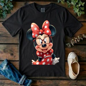 May include: A black short-sleeved t-shirt featuring a graphic of a cartoon mouse wearing red-rimmed glasses and a large red bow with white polka dots. The mouse is also wearing a matching red dress with white polka dots and white gloves.
