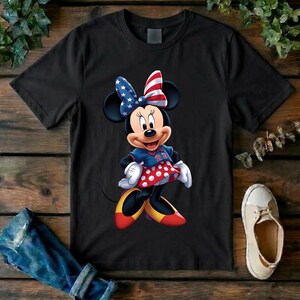 May include: A black short-sleeved t-shirt featuring a graphic of Minnie Mouse wearing a blue jersey with the number 22, a red and white polka dot skirt, yellow shoes, and a bow patterned with the American flag stars and stripes design.