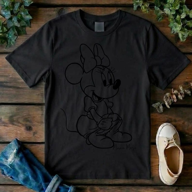 May include: A black short-sleeved t-shirt featuring a minimalist black line art illustration of Minnie Mouse sitting down. The character design includes her signature bow and rounded ears, with the name Minnie Mouse written in script below.