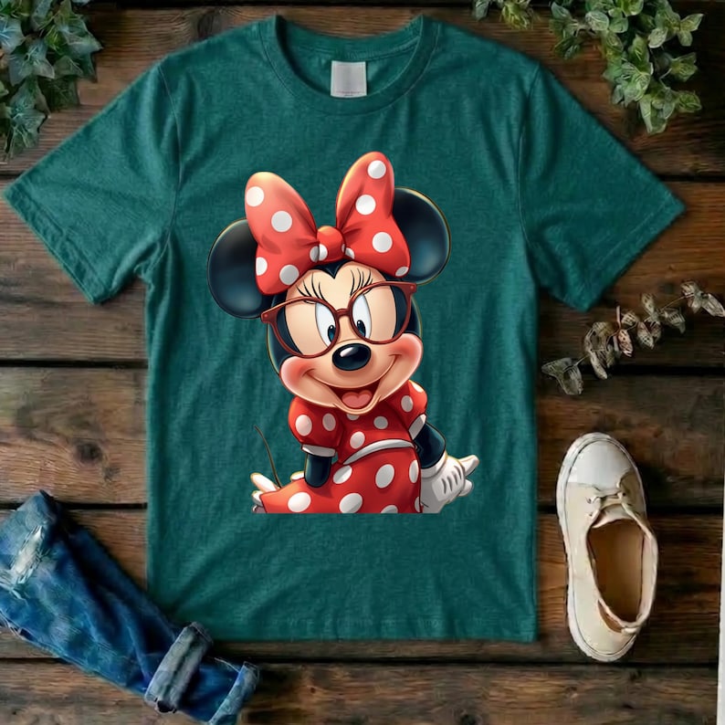 May include: A dark teal short-sleeve t-shirt featuring a graphic of Minnie Mouse wearing red-rimmed glasses and a matching red dress with white polka dots. The character has a large red bow with white polka dots between her black ears.