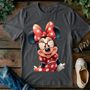 May include: A charcoal gray short-sleeve t-shirt featuring a graphic of Minnie Mouse wearing red-rimmed glasses and a red dress with white polka dots. The character has a large red bow with white polka dots on her head and white gloves.