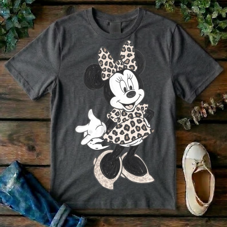 Op de afbeelding: Een donkergrijs t-shirt met korte mouwen en een afbeelding van een tekenfilmmuis. Het personage draagt een jurk en een strik, beide versierd met een beige en zwart luipaardpatroon. De muis heeft zwarte oren en witte handschoenen.