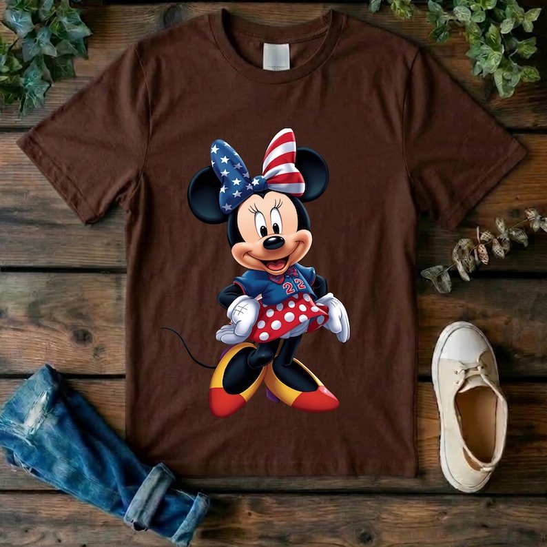 May include: A brown short-sleeved t-shirt featuring a graphic of Minnie Mouse wearing a red, white, and blue star-spangled bow, a blue top with the number 22, and a red skirt with white polka dots, paired with yellow and red shoes.