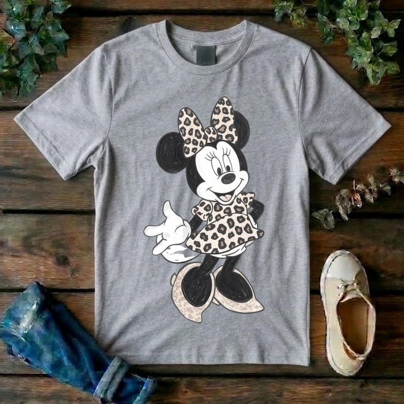 Op de afbeelding: Een grijs gem&ecirc;leerd T-shirt met korte mouwen en een afbeelding van een cartoonmuis. Het personage draagt een jurk en een strik, beide versierd met een bruin en zwart luipaardpatroon. De muis heeft zwarte oren en witte handschoenen.