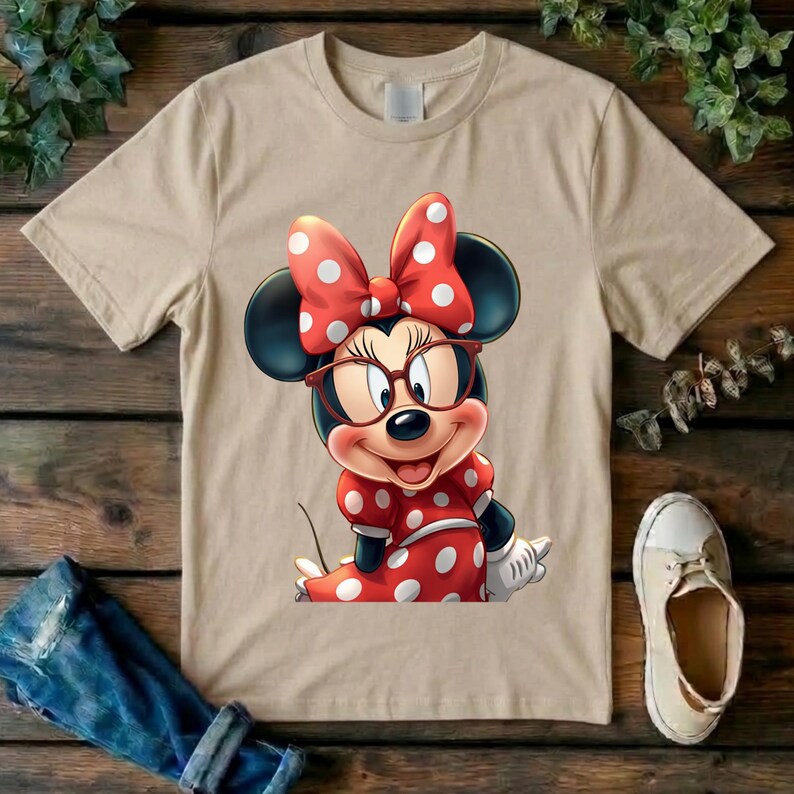 May include: A beige short-sleeved t-shirt featuring a graphic print of a cartoon mouse character wearing red-rimmed glasses and a red dress with white polka dots, topped with a matching red bow with white polka dots on its head.