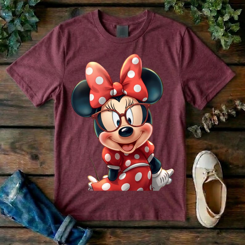 May include: A maroon short-sleeved t-shirt featuring a graphic of Minnie Mouse wearing large brown-rimmed glasses and a red bow with white polka dots. The character is also wearing a matching red dress with white polka dots and white gloves.