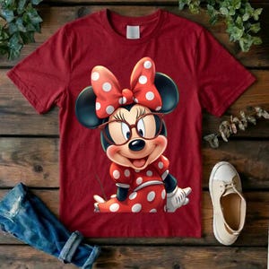 May include: A dark red short-sleeved t-shirt featuring a graphic of a cartoon mouse wearing large brown-rimmed glasses, a red and white polka-dot bow, and a matching red and white polka-dot dress with white gloves on a dark red background.