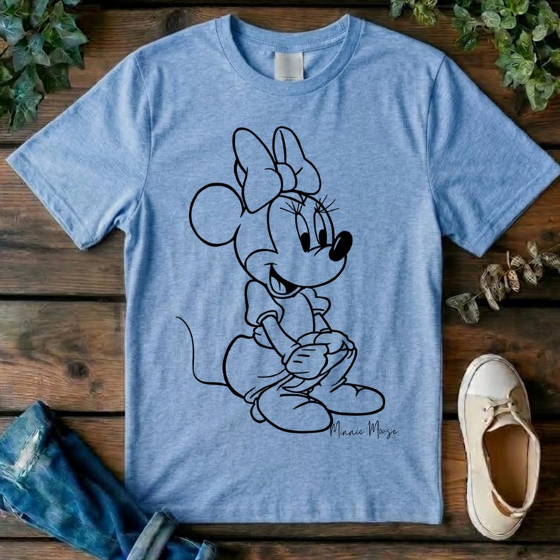 May include: A light blue short-sleeve t-shirt featuring a black line art graphic of Minnie Mouse sitting down. The character is depicted with her signature bow and dress. The design is centered on the chest of the garment, which has a crew neckline.