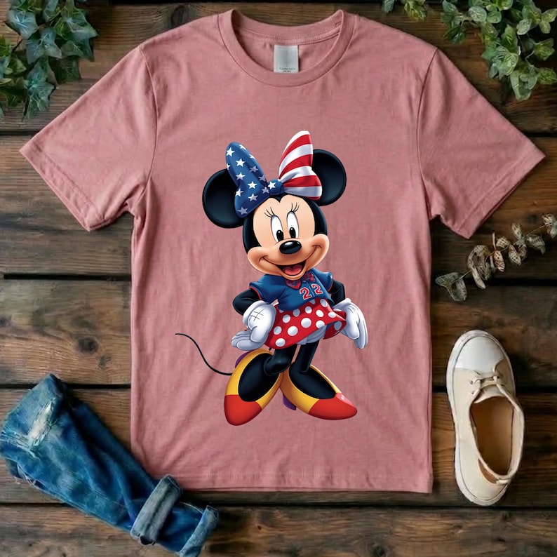 May include: A dusty rose short-sleeved t-shirt featuring a graphic of a cartoon mouse wearing a blue and red star-patterned bow, a blue jersey with the number 22, and a red skirt with white polka dots, paired with yellow and red shoes.