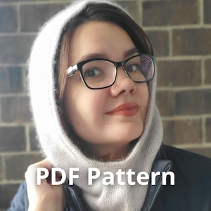 May include: A light gray knitted hood with the text "PDF Pattern" in white. The hood is worn by a person wearing black glasses and a dark jacket. The background is a brick wall.