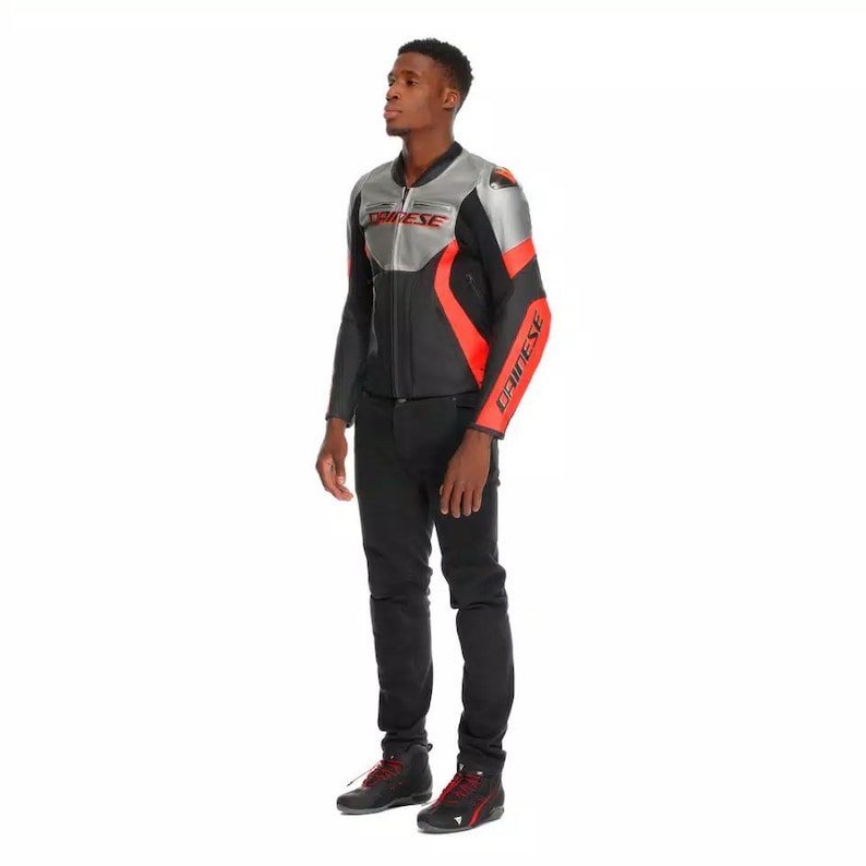 May include: A black and silver motorcycle jacket with red accents. The jacket has the brand name "DAINESE" printed on the chest and sleeves. The person in the image is wearing black pants and black shoes.