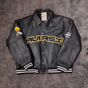 May include: Black leather jacket with the word "AVIREX" in yellow across the chest. The jacket has a button-up front, a collar, and white stripes on the cuffs and hem. Patches are on the sleeves.