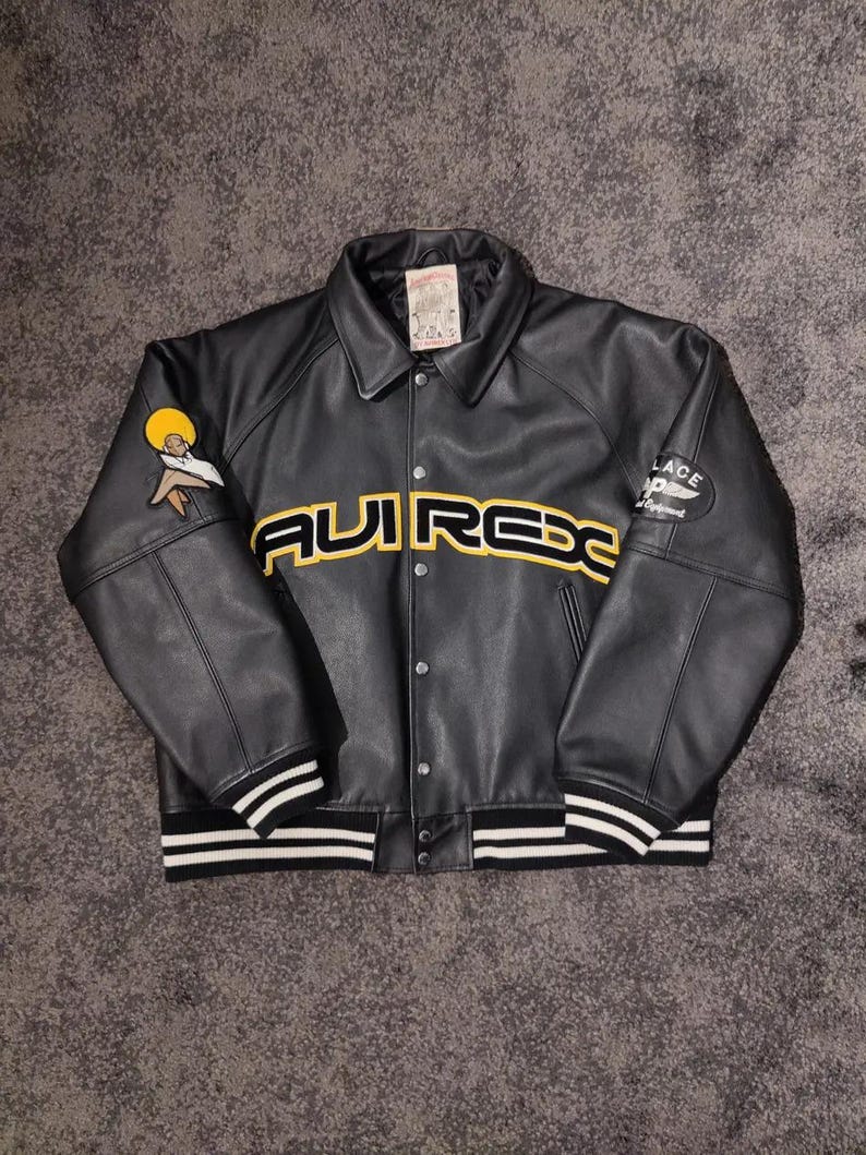 May include: Black leather jacket with the word "AVIREX" in yellow across the chest. The jacket has a button-up front, a collar, and white stripes on the cuffs and hem. Patches are on the sleeves.