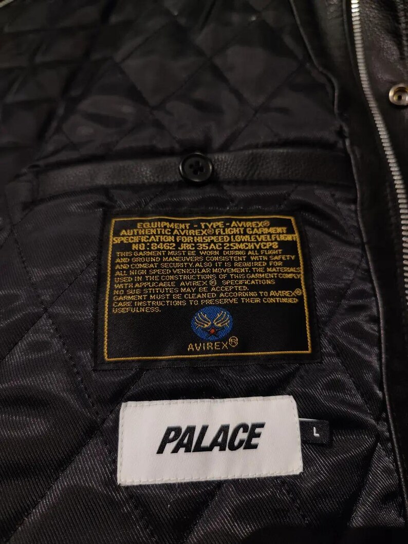 May include: Black leather jacket interior with a quilted lining. Features labels with "AVIREX" and "PALACE" branding. The jacket has a button closure and a size "L" tag.