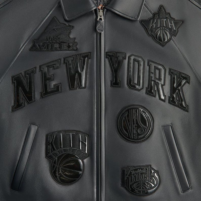 May include: Black leather jacket with the text "NEW YORK" across the chest. The jacket features multiple patches, including "KITH" and basketball-themed designs. A zipper runs down the center.