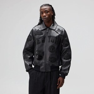 May include: Black leather jacket with multiple patches and the text "NEW YORK" across the chest. The jacket has a zip-up front, a collar, and ribbed cuffs and hem. Patches include basketballs and other sports-related designs.