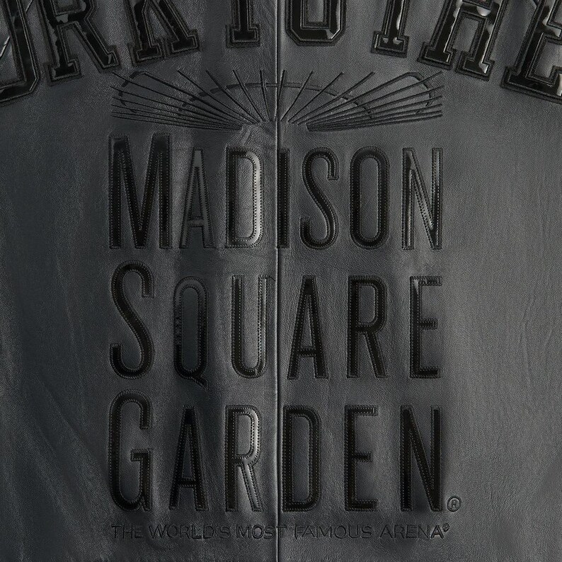May include: Close-up of a black leather jacket with the embossed text "MADISON SQUARE GARDEN." The text is in a bold, serif font. Below the text is the phrase "THE WORLD'S MOST FAMOUS ARENA." The jacket has a textured surface.