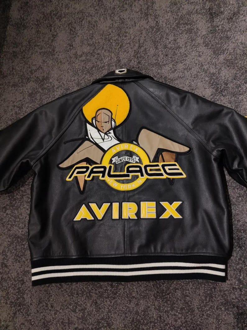May include: Black leather jacket with a large graphic on the back. The graphic includes a stylized figure, the word "PALACE" in yellow, and the "AVIREX" logo. The jacket has a striped hem.