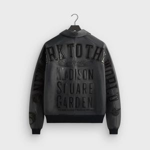 May include: Black leather jacket with the text "NEW YORK TO THE WORLD" and "MADISON SQUARE GARDEN" embossed on the back. The jacket has a black ribbed hem and cuffs, and a collar. The text "THE WORLD'S MOST FAMOUS ARENA" is also visible.
