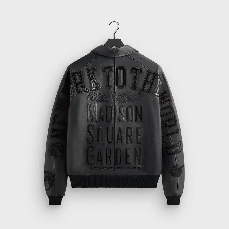 May include: Black leather jacket with the text "NEW YORK TO THE WORLD" and "MADISON SQUARE GARDEN" embossed on the back. The jacket has a black ribbed hem and cuffs, and a collar. The text "THE WORLD'S MOST FAMOUS ARENA" is also visible.