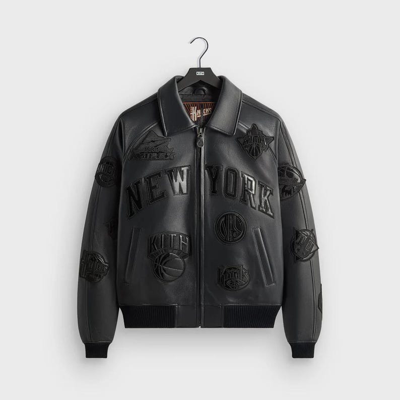 May include: Black leather bomber jacket with multiple patches and the words "NEW YORK" across the chest. The jacket has a zip-up front, a collar, and ribbed cuffs and hem. Patches include basketball-related designs and the Kith logo.