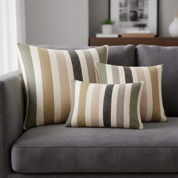 Può includere: Tre cuscini decorativi rettangolari caratterizzati da un motivo a righe verticali nei toni del verde oliva, beige, crema e grigio antracite scuro. I cuscini sono disposti in gruppo, con un grande cuscino quadrato e due più piccoli.