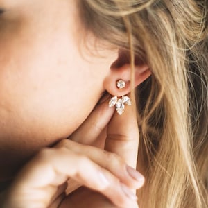 Puede incluir: Pendientes de oro con un racimo de cristales transparentes. Los pendientes tienen un pequeño botón redondo y un racimo más grande de cristales que cuelgan debajo.