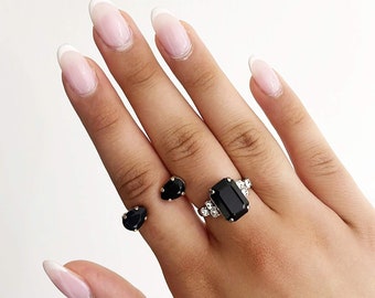 May include: A set of two black gemstone rings. One ring features a large rectangular black gemstone with smaller clear gemstones around it. The other ring has two smaller black gemstones.