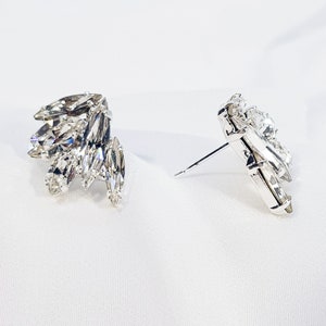 May include: A pair of silver earrings featuring clear crystal stones. The earrings are designed in a cluster of marquise-shaped stones.