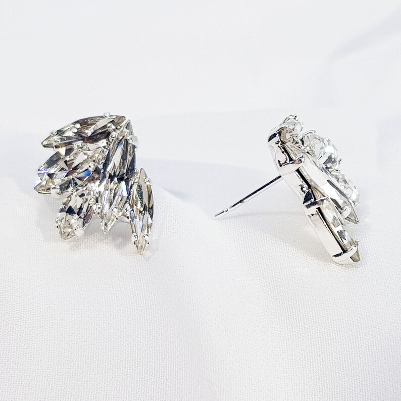 May include: A pair of silver earrings featuring clear crystal stones. The earrings are designed in a cluster of marquise-shaped stones.
