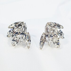 May include: A pair of silver-tone earrings featuring a cluster of clear marquise-shaped crystals. The crystals are arranged in a fan shape.